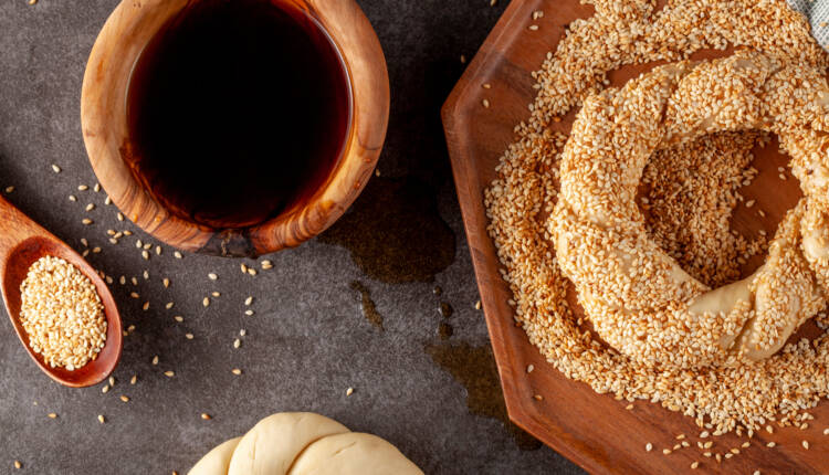 delicious Turkish bagel with sesame seeds known as susamli simit.  Woman baker is making it using twisted dough dipped into a bowl of pekmez and sesame seeds.