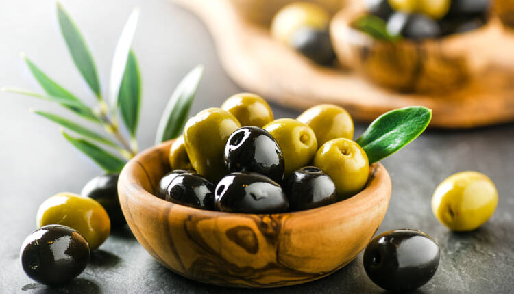Fresh olives with core in olive bowl on dark stone table and gre